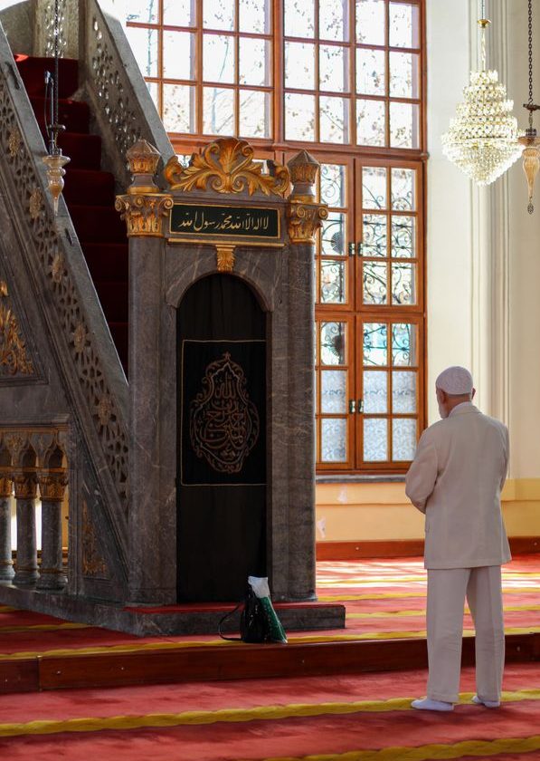A man prays inside a beautifully decorated mosque bathed in natural sunlight.