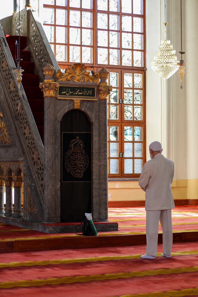 A man prays inside a beautifully decorated mosque bathed in natural sunlight.