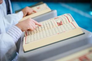 Focused image of hands reading the Quran opened to a page with Arabic script.